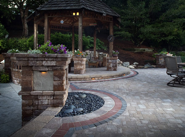 Backyard landscape with loose rocks, patio table, and rustic gazebo.