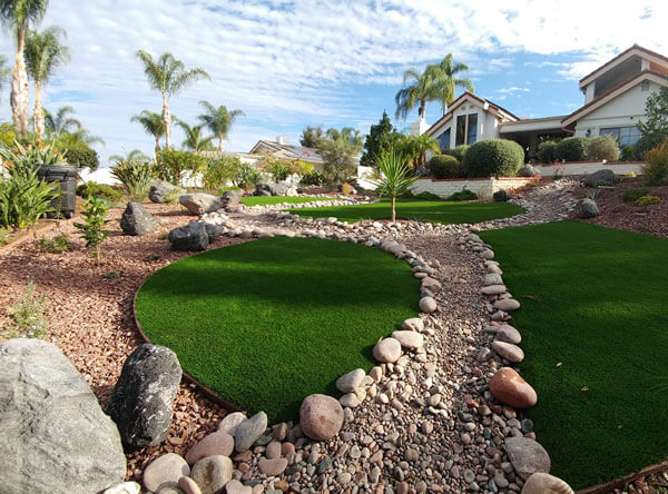 Tiki inspired backyard with artificial grass and loose stones.