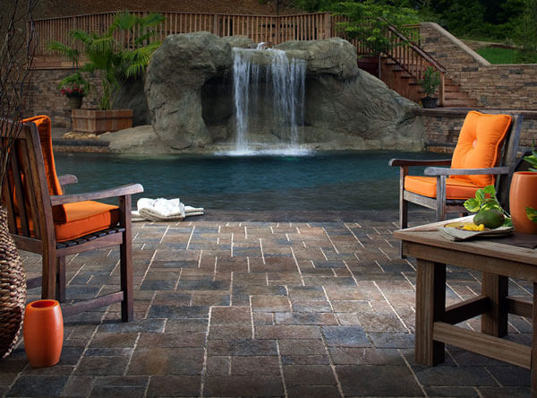 Backyard pool area with a waterfall and paving stones.