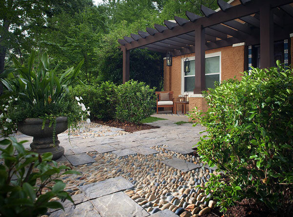 Patio with loose stones set with concrete and pavers, with a dark brown pergola.