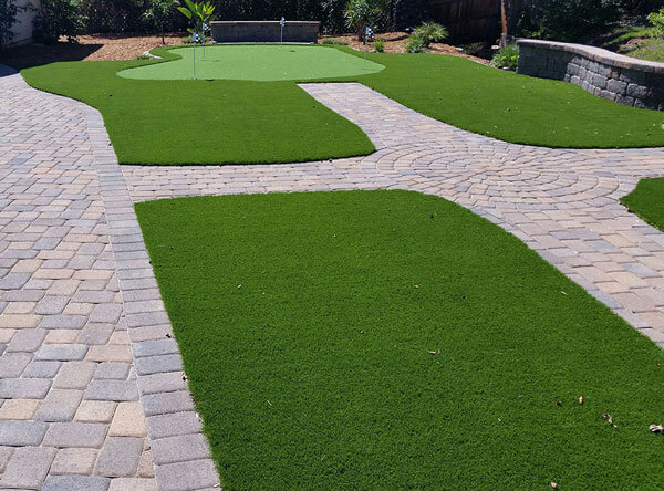 Putting green with artificial grass areas next to a pool.