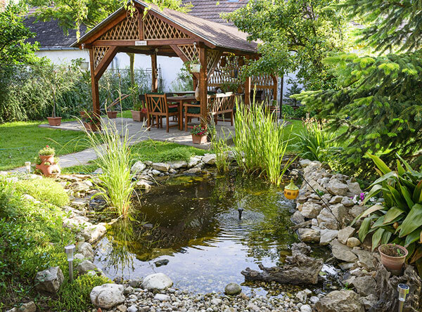 A small pond next to a beautiful garden with bench.
