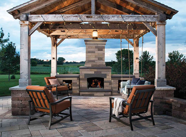 A gazebo covering an outdoor patio area with bench swing and outdoor fireplace.