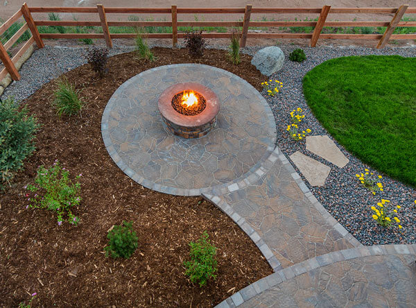 Outdoor firepit surrounded with pavers and tree bark.