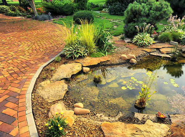 Pond next to red pavers and loose stones.