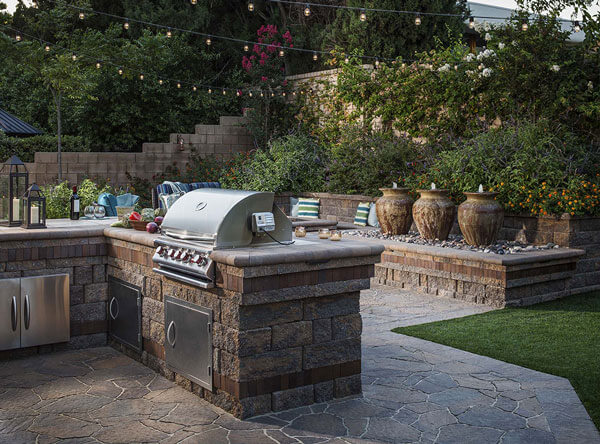 Paving stones laid down next to an outdoor kitchen and jar fountains on a raised wall bed.
