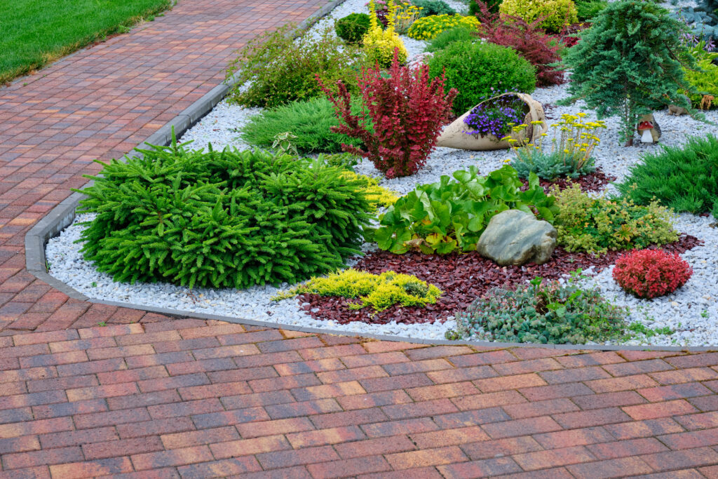 Backyard landscaping with bright green plants in gravel and a brick walkway. 