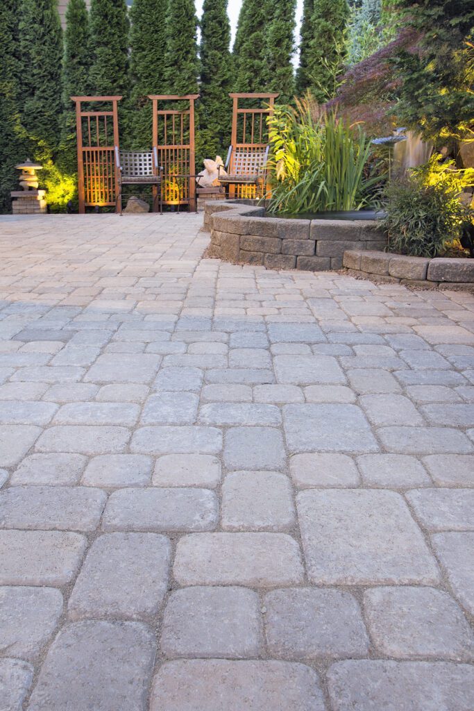 Backyard with different sized pavers, stone walls with planters, and greenery. 