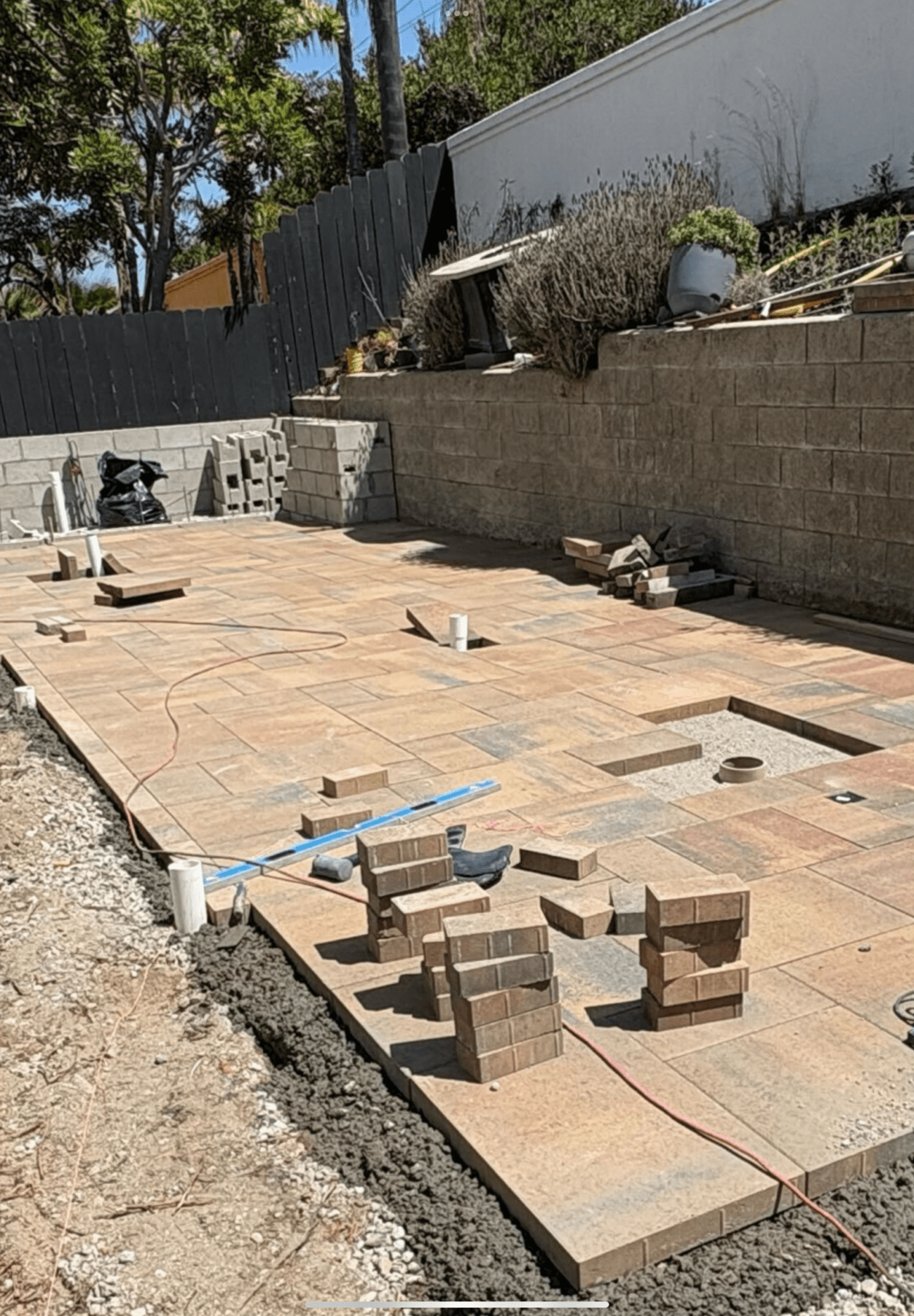 Partially laid tan paver patio under construction with stacked pavers, open cutouts, and a red guide string in an Encinita...