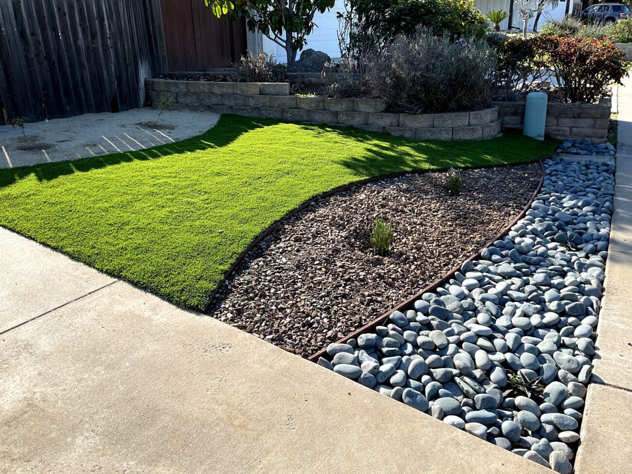 Front yard shows a completed landscaping installation with newly laid artificial turf bordered by a curved planting bed...