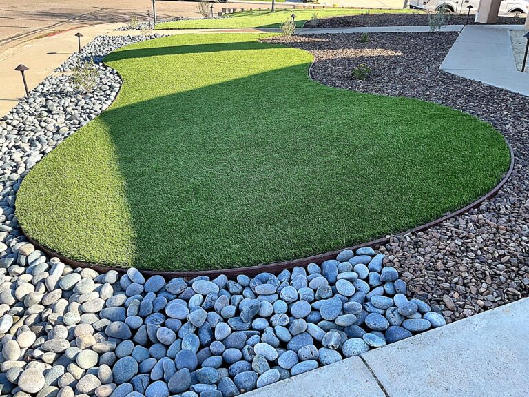 The finished front yard: artificial turf edged in metal border meets a river-rock mulch bed, with curved turf beds...