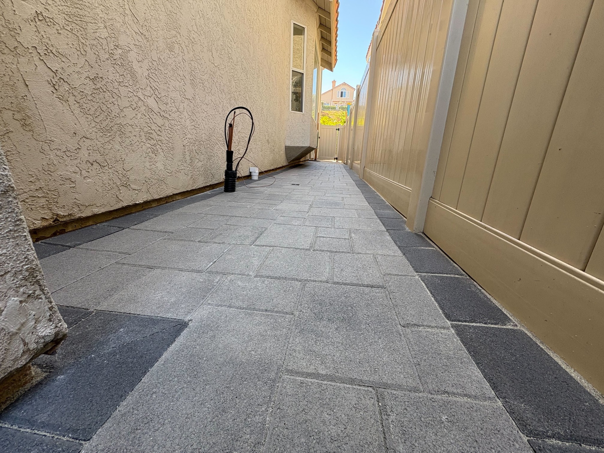 Narrow side-yard passage with freshly laid gray rectangular pavers and a darker soldier-course border along both edges.