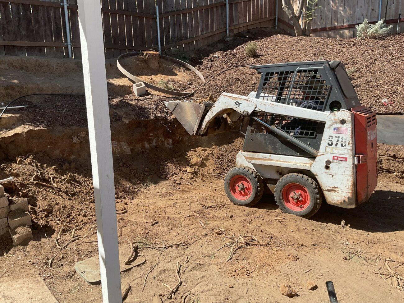 Bobcat S70 skid-steer loader excavating soil in a residential backyard during demolition and grading work.