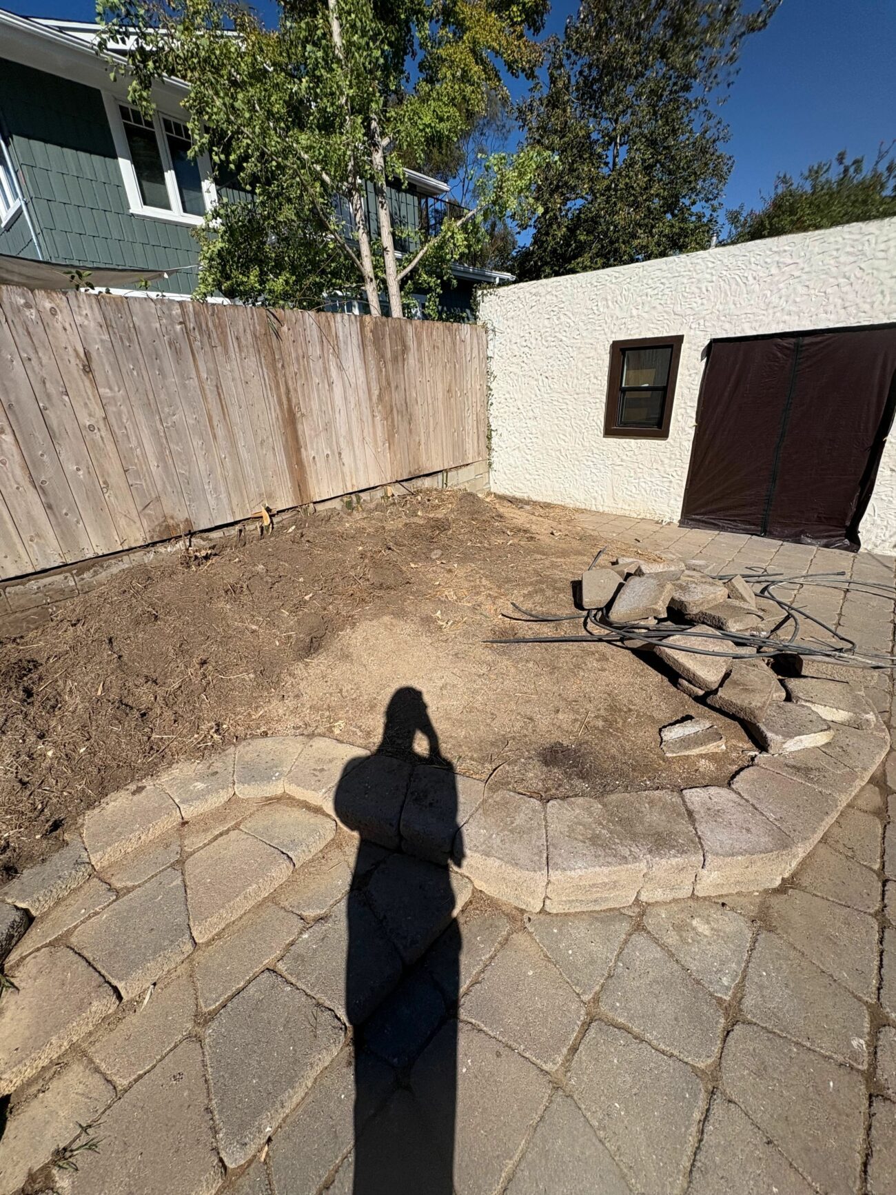 Cleared backyard with bare soil, a partial segmental retaining wall, and an existing paver patio before renovation work be...