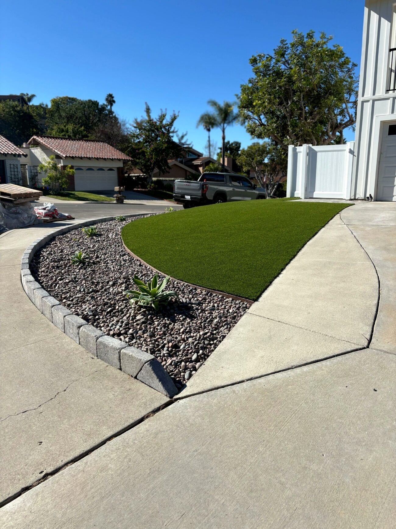 Front yard showing newly installed artificial turf with a curved segmental block edging and rock mulch planting bed...