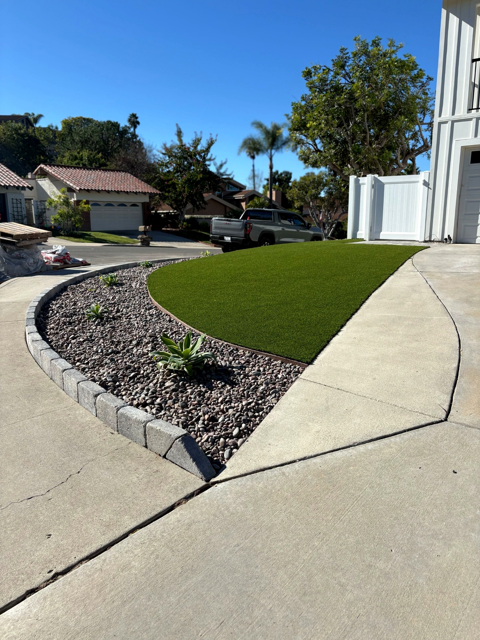 Front yard showing newly installed artificial turf with a curved segmental block edging and rock mulch planting bed...