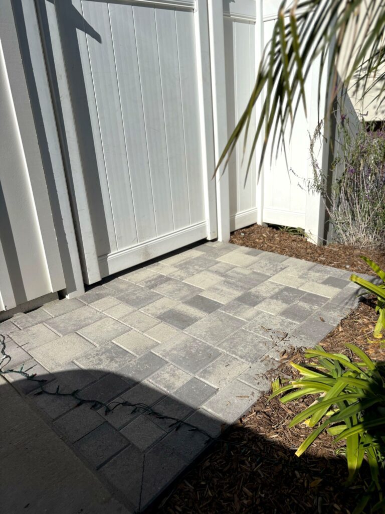 A matching interlocking-paver pad finishes the base of the rear gate where the walkway meets the planting bed.