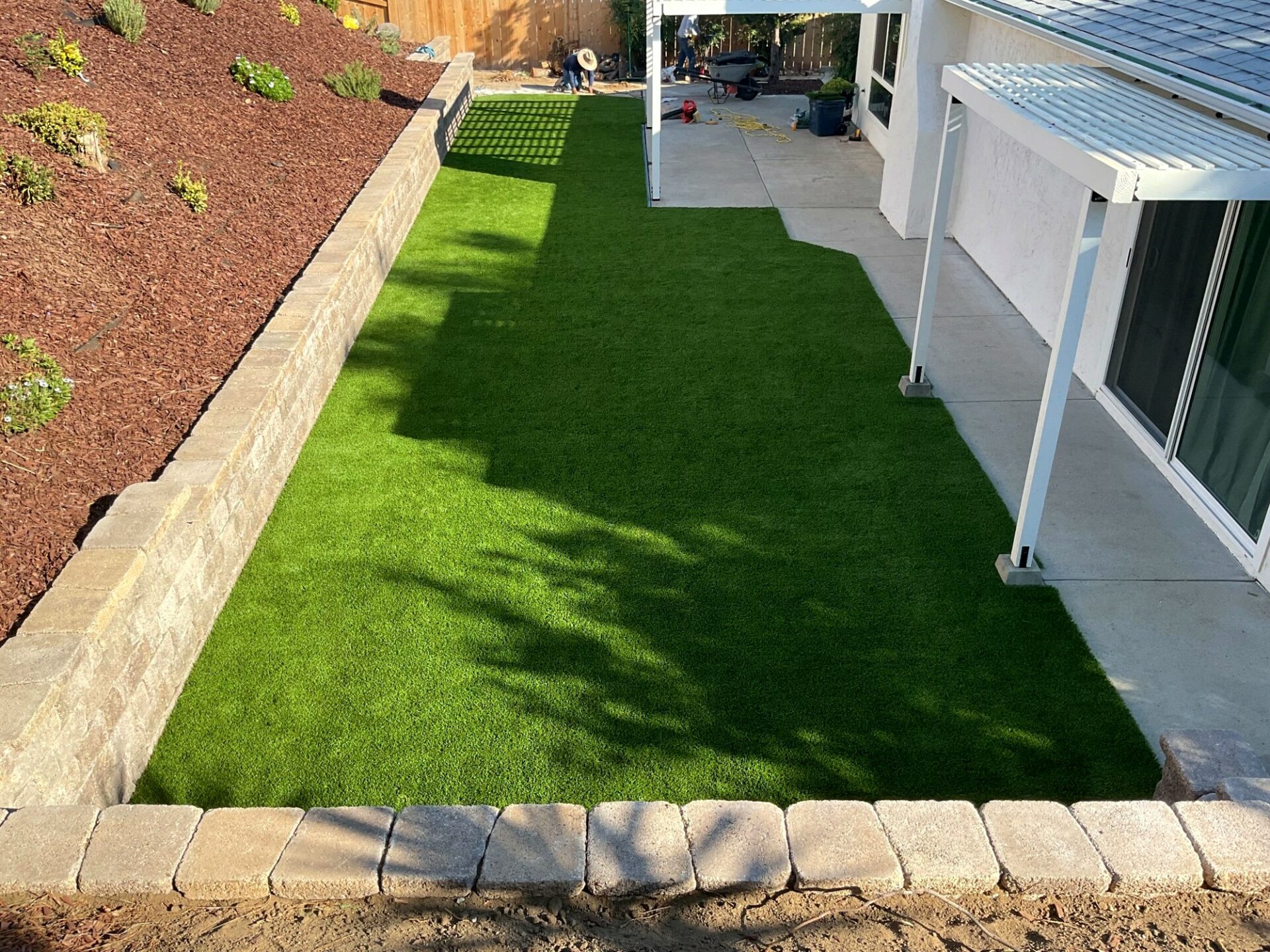 Freshly installed synthetic turf lawn bordered by a segmental retaining wall with cap units and concrete patio in El Cajon.