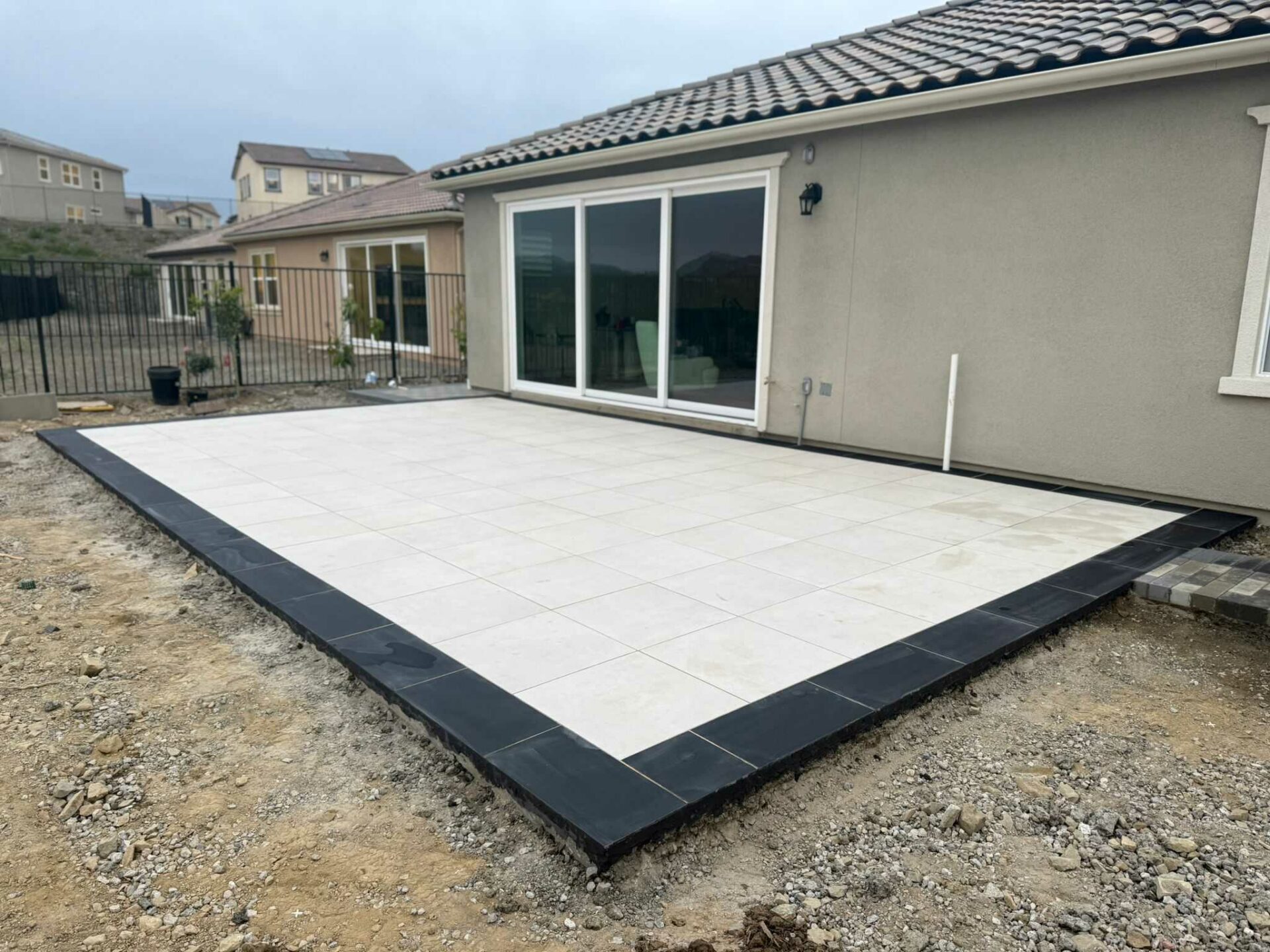 Large-format cream porcelain-style paver patio with a charcoal border, converging on the home's rear sliding glass doors.