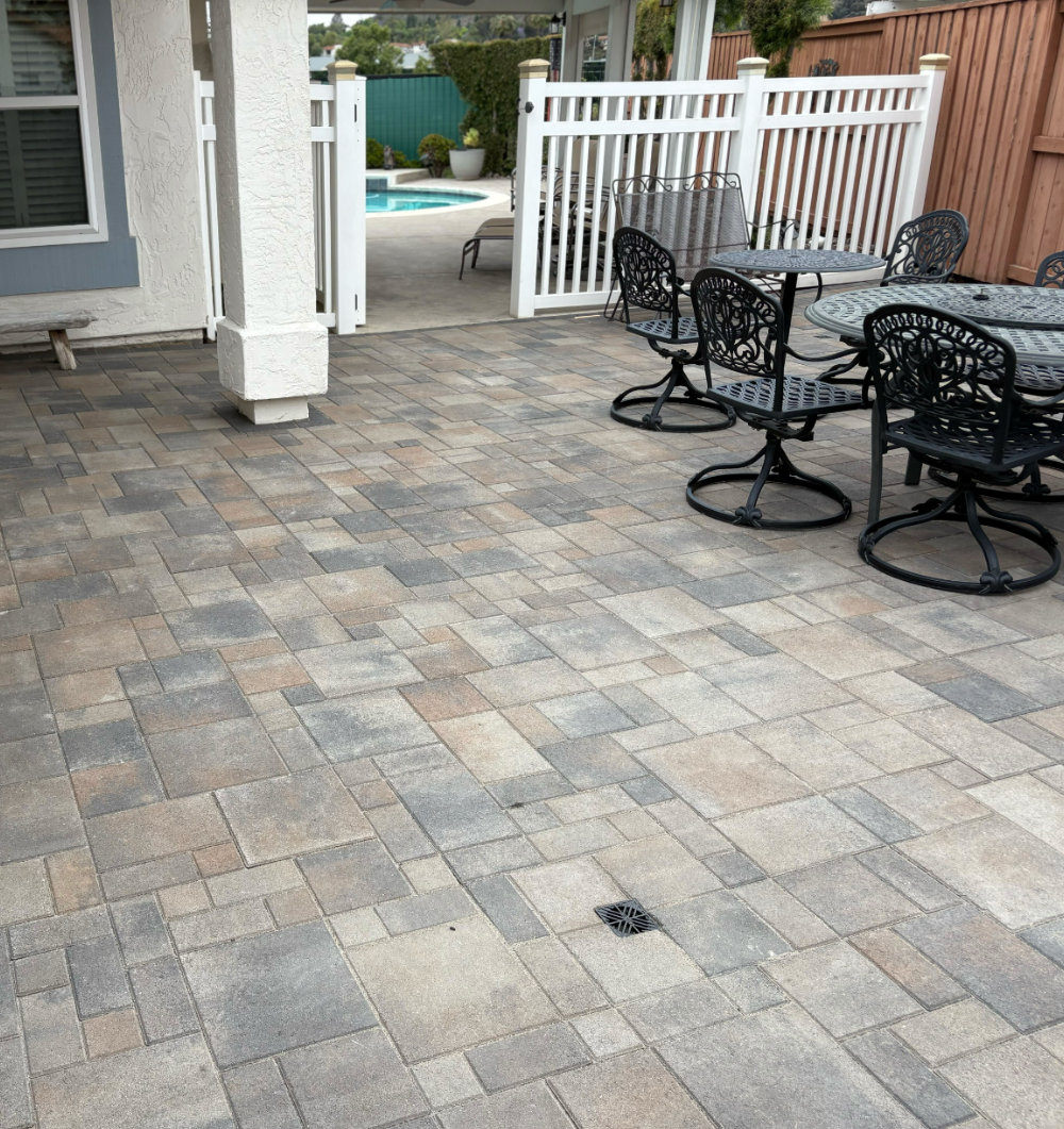 The finished backyard patio in ORCO Villa Express pavers, a flush drain grate set into the field to carry water off the surface.
