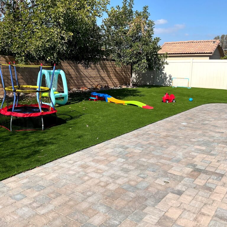 Backyard in Santee with tumbled paver patio beside synthetic turf lawn holding a trampoline, toddler slide, and ride-on toy.
