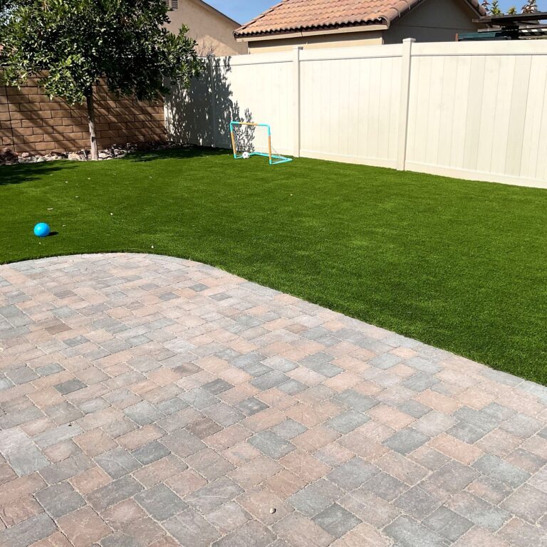 Backyard in Santee with tumbled cobble pavers curving into lush synthetic turf, a small soccer goal, and a tree near the f...
