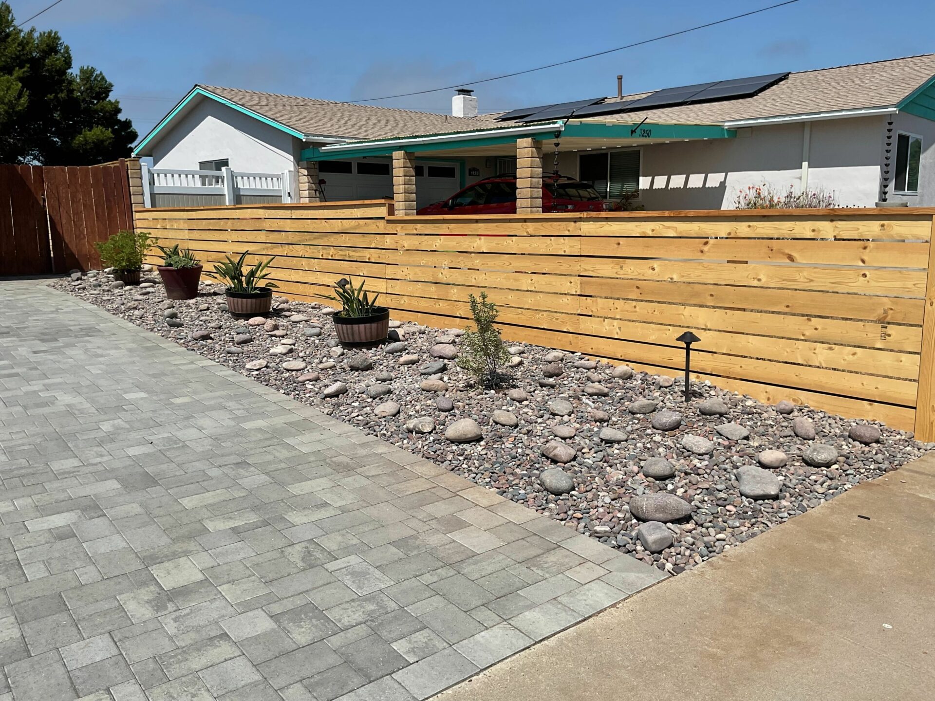 Horizontal cedar fence beside a river rock planting bed with potted succulents and a paver driveway in San Diego.