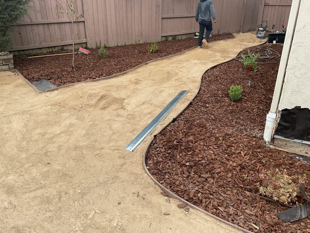 Decomposed granite path base compacted between curved metal edging and shredded fir mulch beds with small shrubs freshly p...