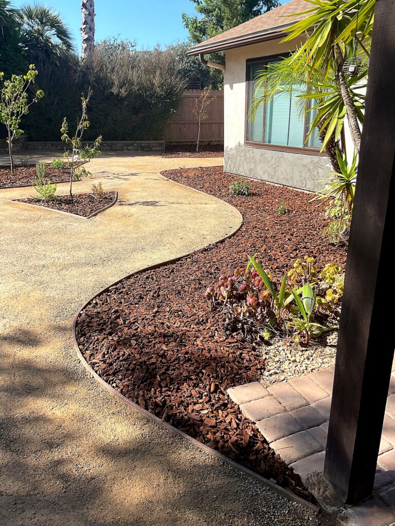 Curved stabilized DG path bordered by shredded fir mulch beds with succulents, beside a stucco home with a yucca tree.