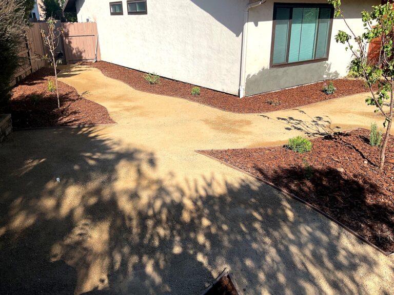 Freshly installed stabilized DG path curves past shredded fir mulch beds and young trees along a white stucco house.