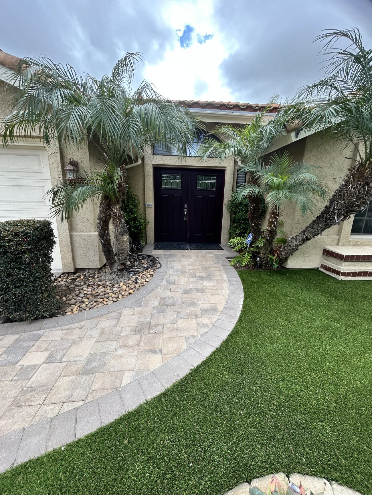 The curved paver walkway and soldier-course border leading to the front door, new turf lawn to the right.
