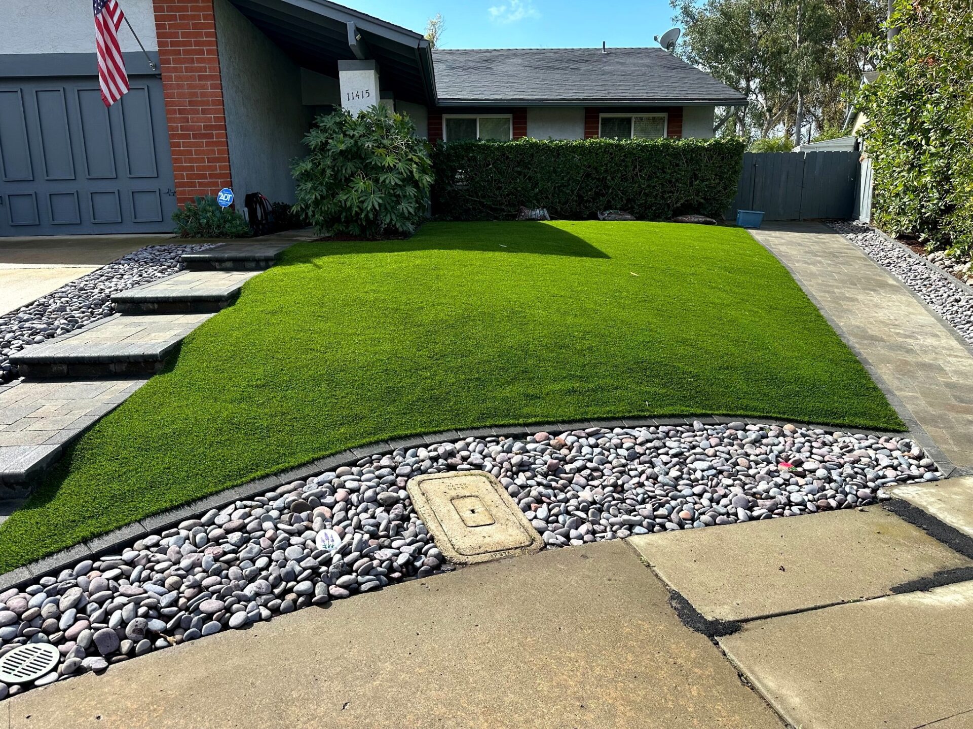 Wide Tierrasanta 92124 front yard with SiteOne Rye turf, ORCO paver walkway, bullnose steps, and river-rock drainage border.