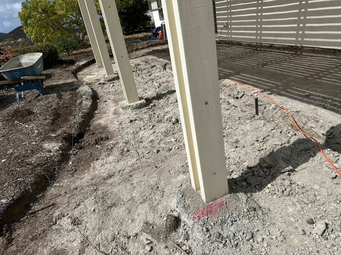 Pergola posts set in compacted gravel base with orange safety fencing, drain stub-outs, and trenching visible during site...