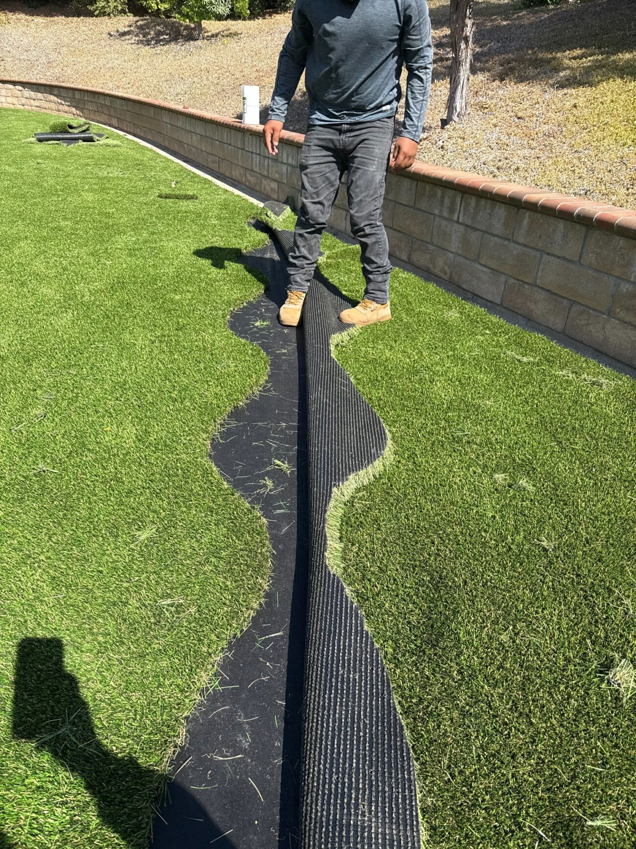 Installer standing at the seam between two sections of rolled synthetic turf, backing visible, during mid-installation.