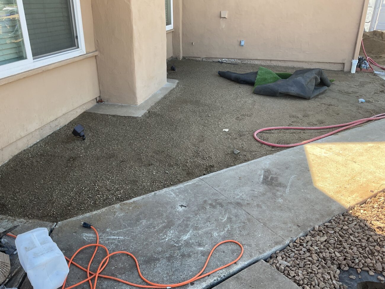 Residential backyard showing a compacted aggregate base prepared against an existing concrete patio, ready for final...