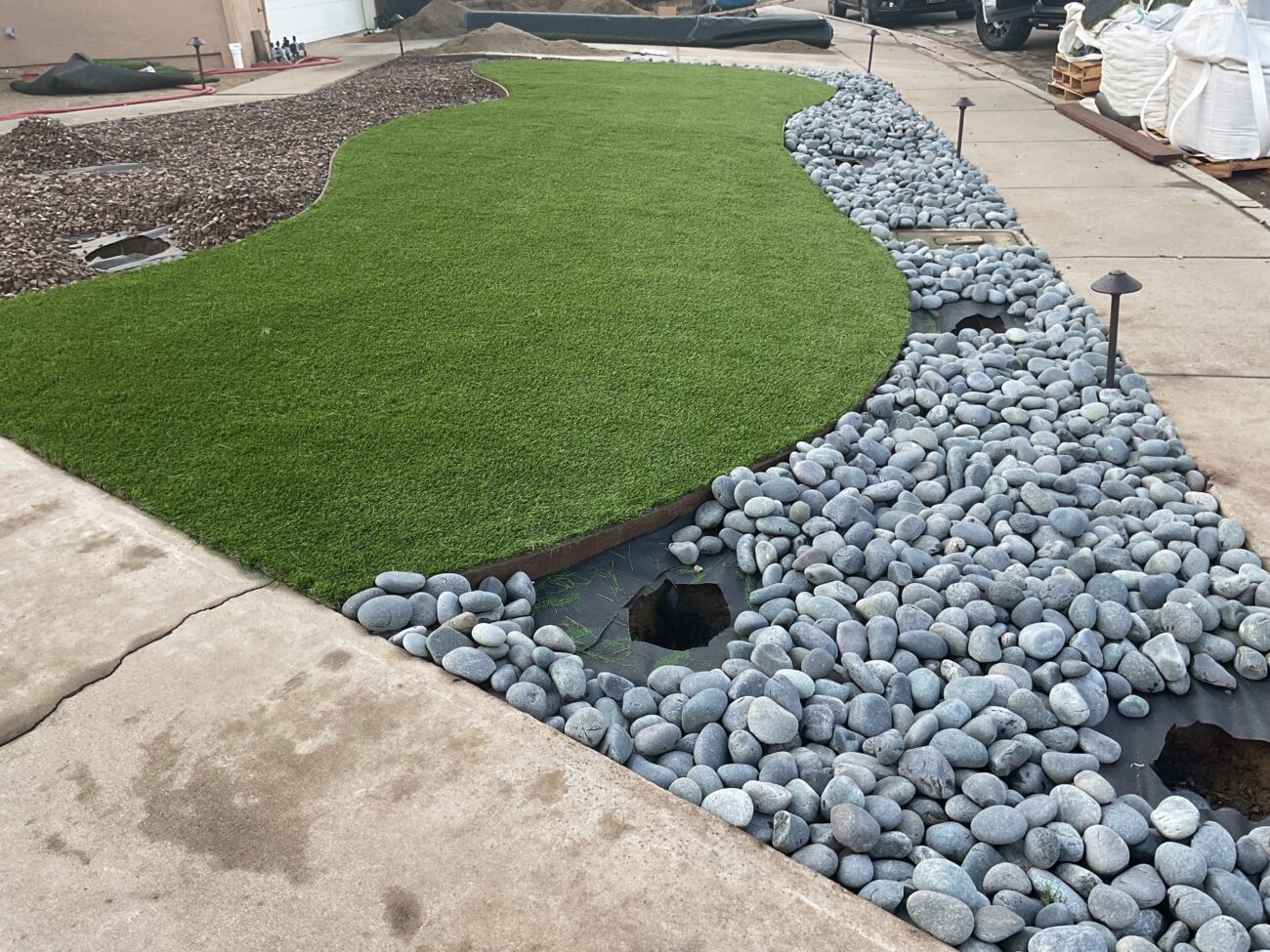 Residential landscape under active installation showing a curved artificial turf area edged with metal landscape edging...