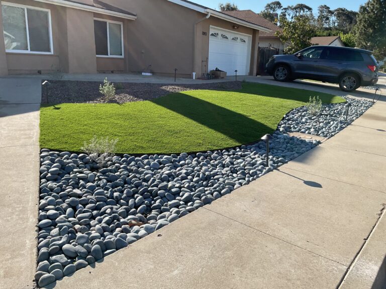 Front yard shows a completed landscape installation with two artificial turf islands separated by a decorative river rock...