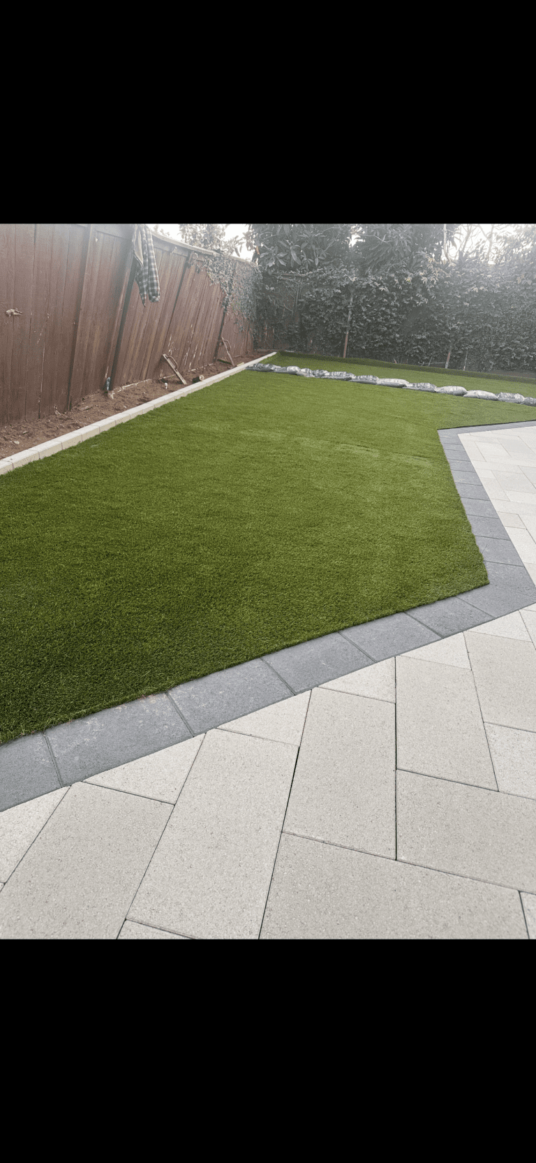 Newly installed artificial turf lawn bordered by a contrasting interlocking paver patio and walkway. Large-format...