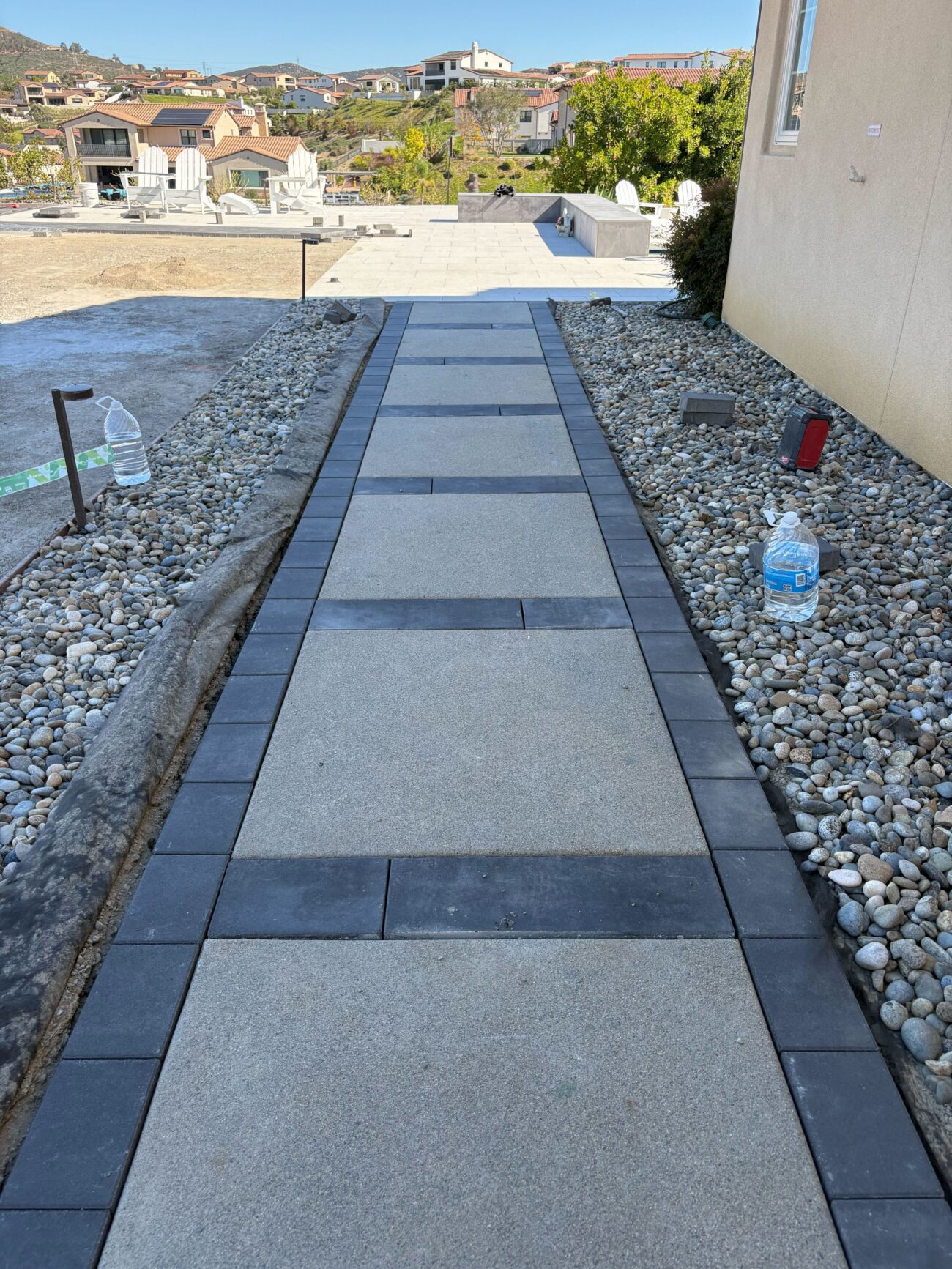 Residential walkway under installation comprised of large-format concrete pavers with a dark soldier-course border and...