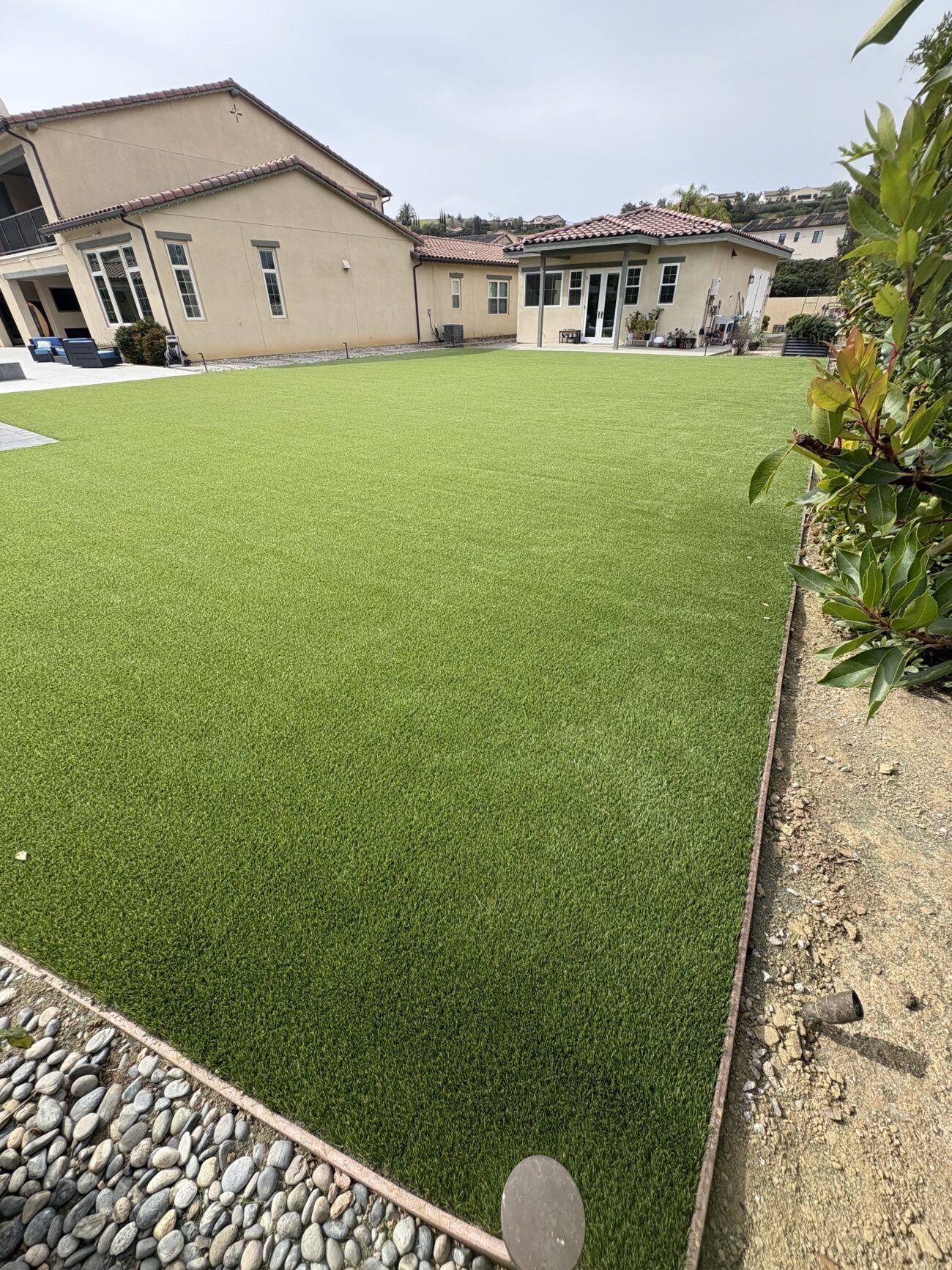 Completed artificial turf installation across a residential backyard showing a uniform turf field with a defined edge...