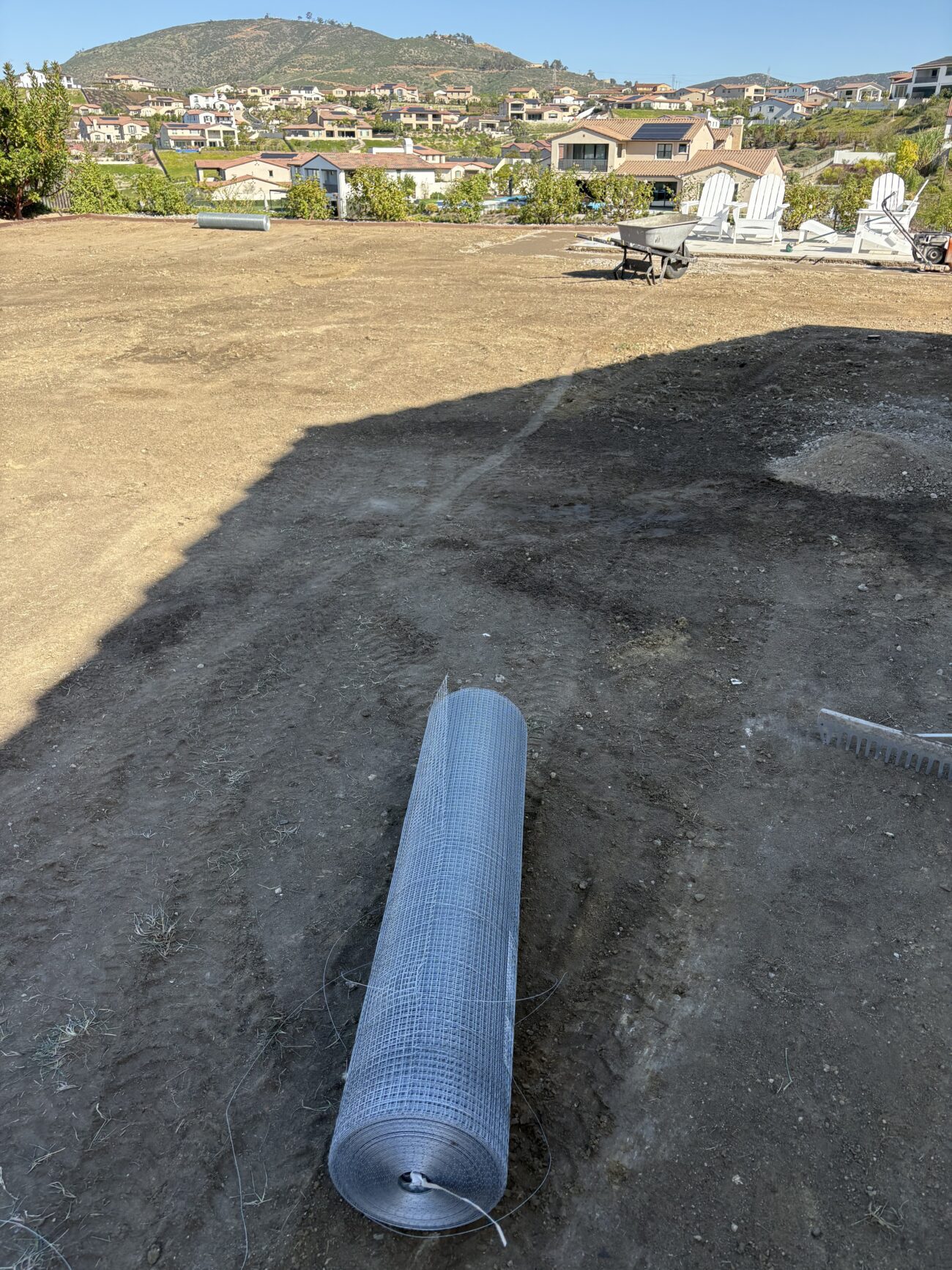 Cleared residential backyard showing rough grade and compacted soil with a large roll of wire mesh or erosion control...