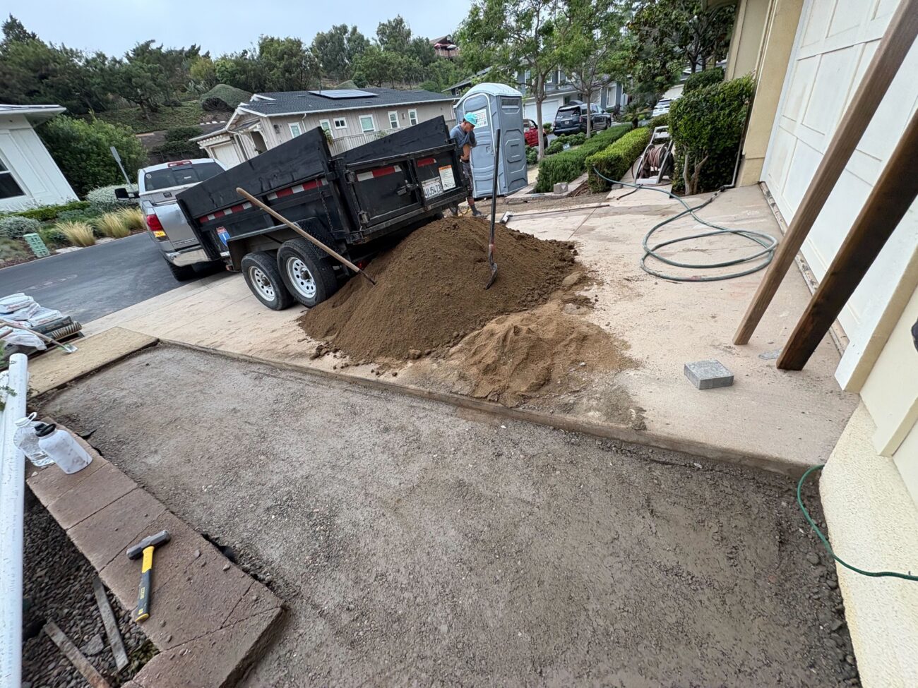 Residential front-drive work area showing a prepared paver base/compacted aggregate section adjacent to a concrete apron....