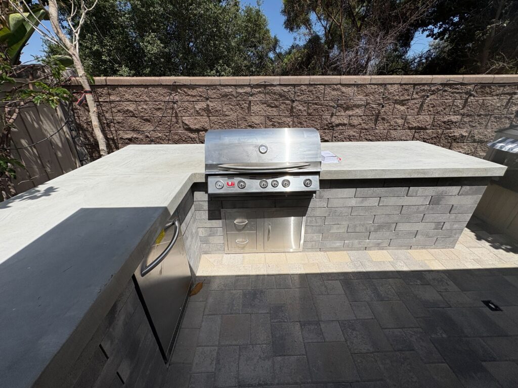 Residential outdoor kitchen with a stainless steel built-in grill set into a concrete countertop and concrete block...