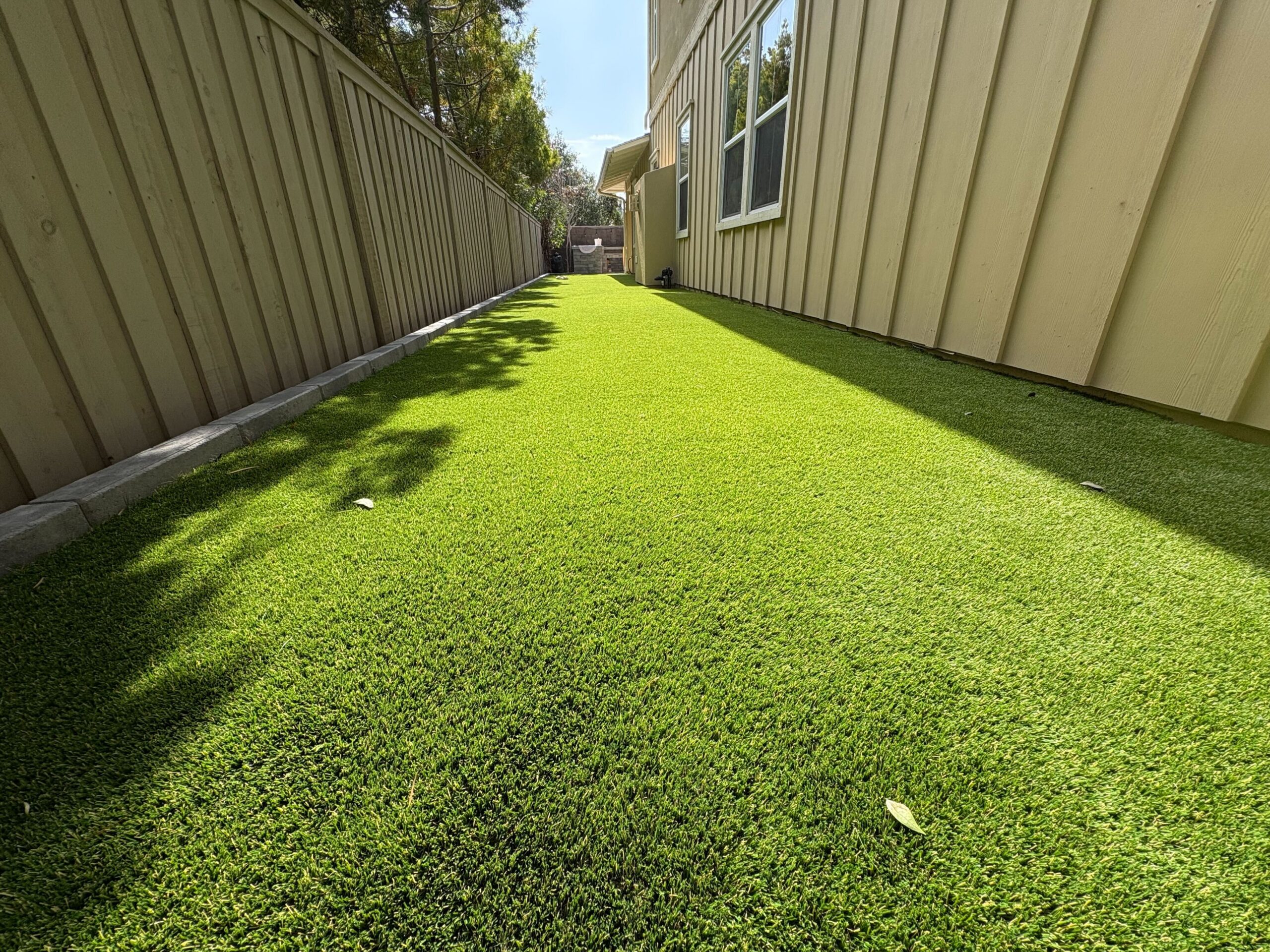 Narrow side yard finished with artificial turf and a clean concrete edge along the fence.
