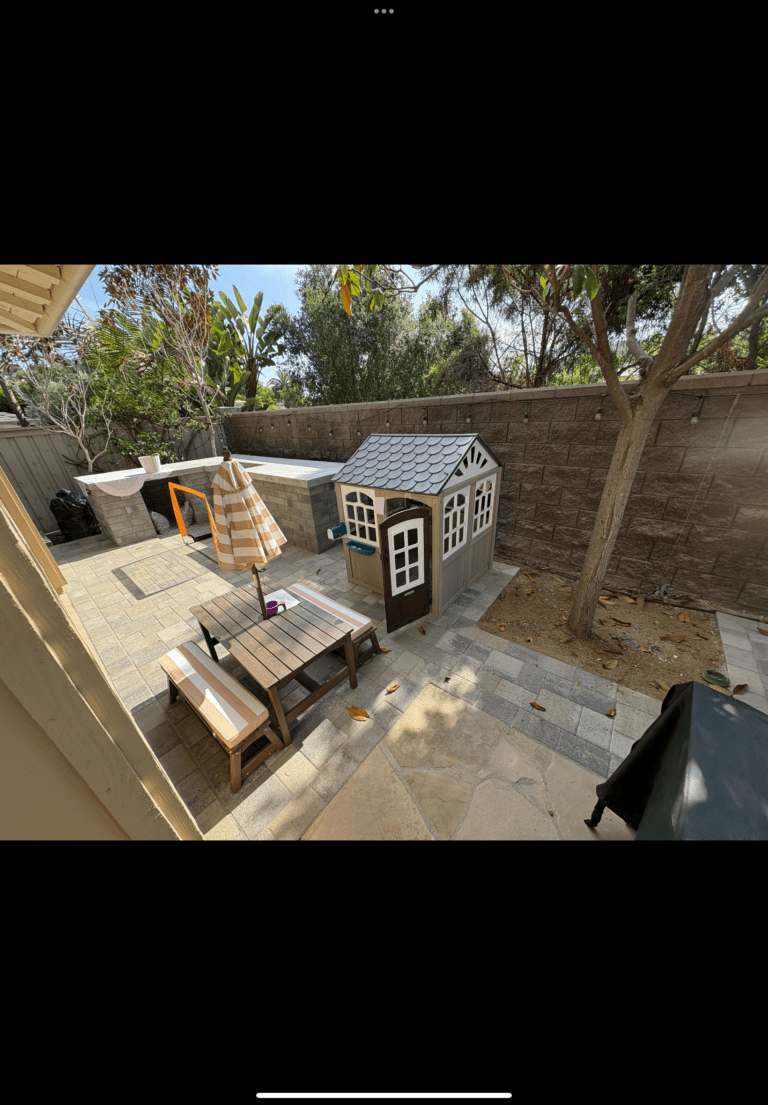 Backyard shows a newly installed interlocking paver patio with bench seating and a small children's playhouse next to a...