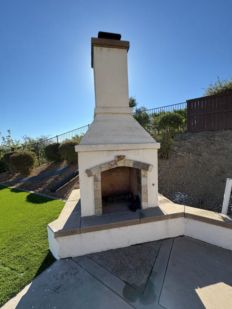 Completed masonry outdoor fireplace with a tall chimney and concrete cap set on a finished concrete/paver patio adjacent...
