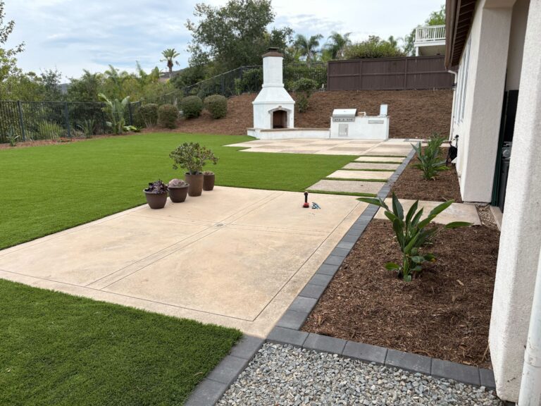 Finished backyard landscape showing an artificial turf lawn with large concrete stepping pavers leading to a built-in...
