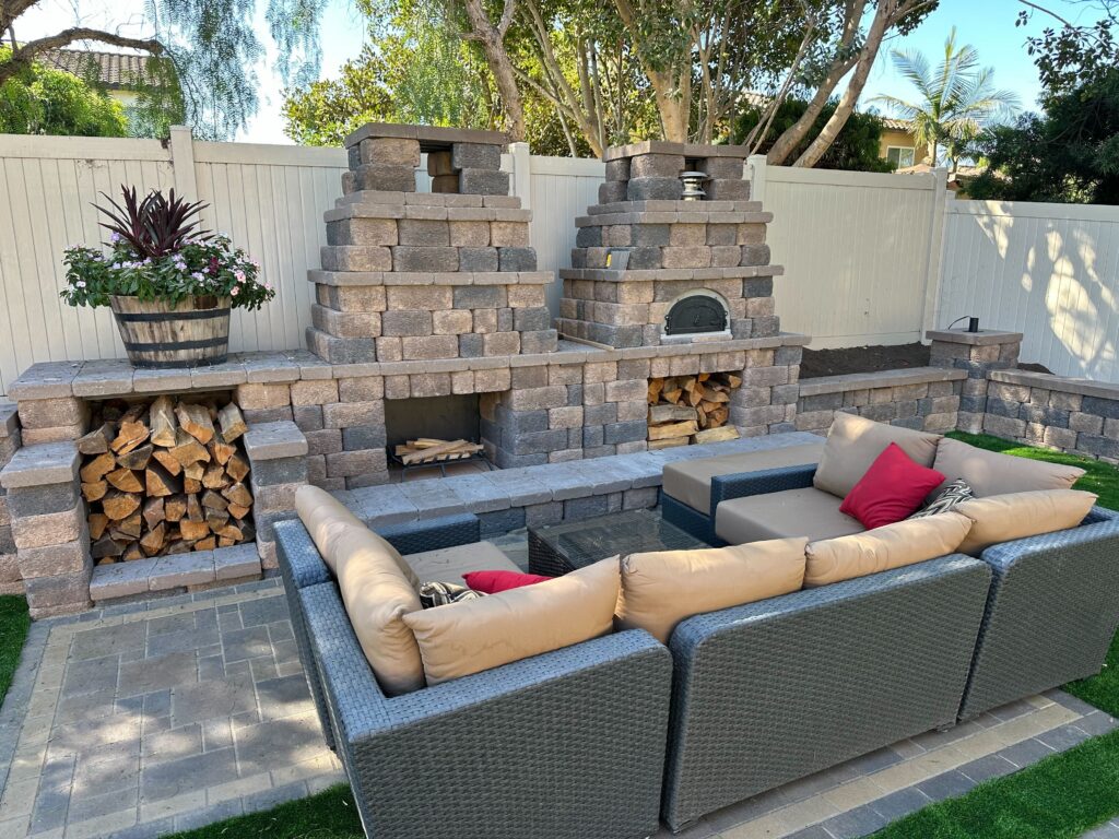 Finished backyard outdoor living area featuring a paver patio with a multi-functional segmental block wall that houses a...
