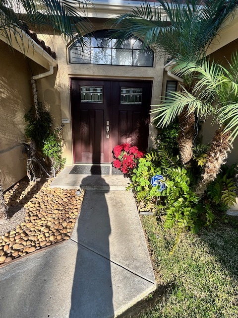 Original front entry with a plain straight concrete walkway leading to double doors, flanked by a river-rock bed and existing plantings.