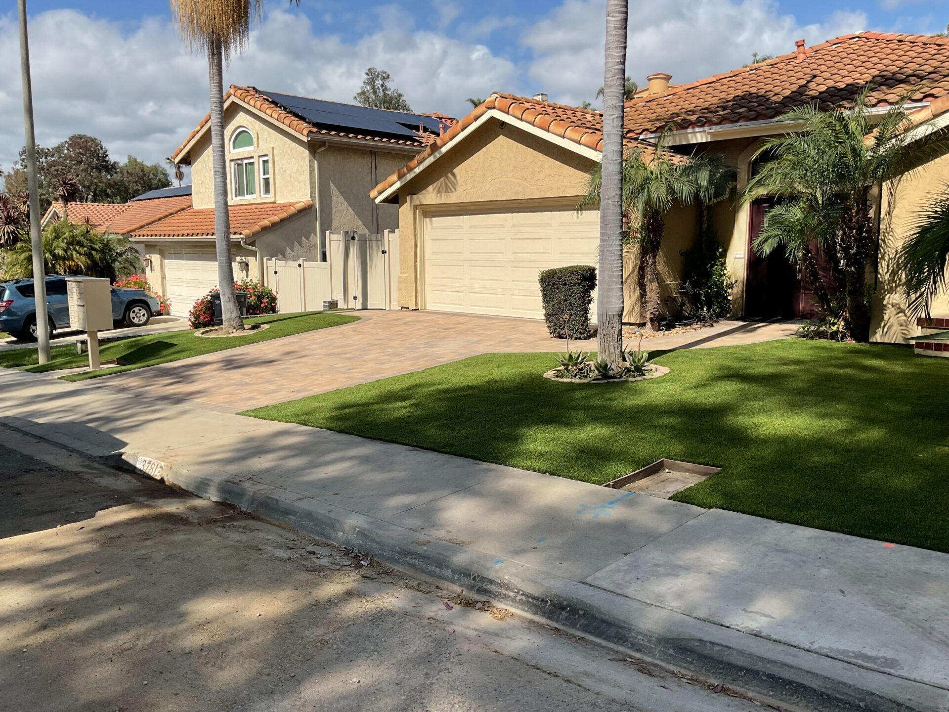 Residential front yard showing a recently completed interlocking paver driveway with adjacent artificial turf....